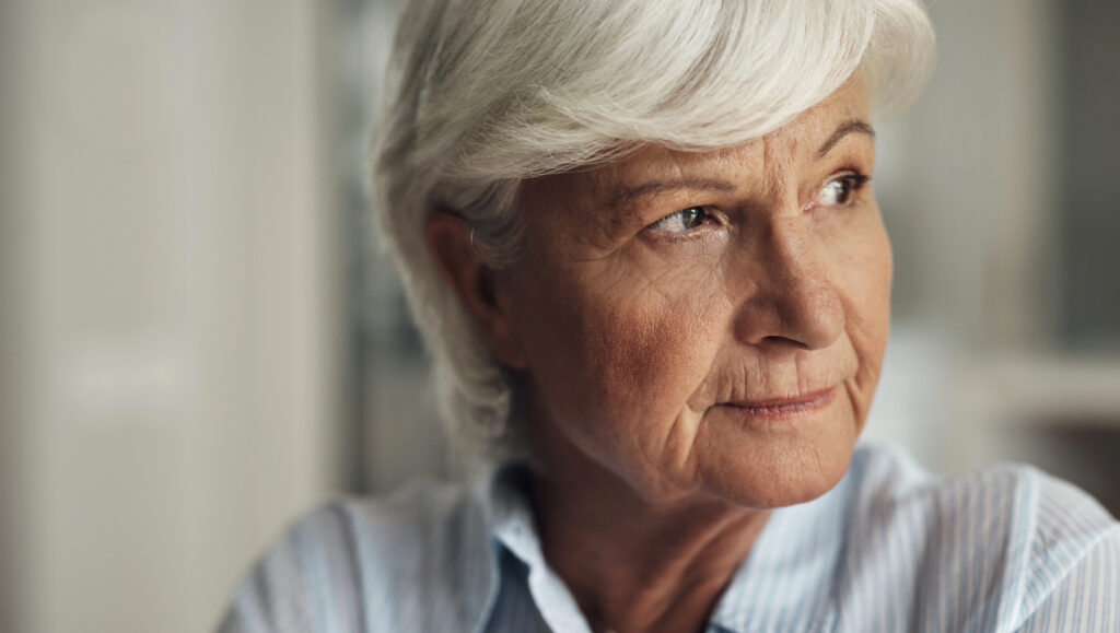 Ältere Mutter schaut nachdenklich aus dem Fenster – Kontaktabbruch zum erwachsenen Kind